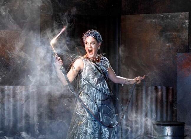 kvinna i dramatisk operamiljö sjunger för fulla muggar i en pompös klänning