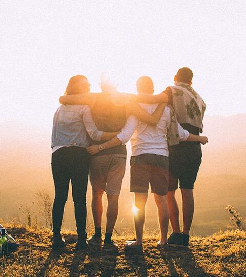 Vänner håller om varandra framför en solnedgång och en bra utsikt över en äng. 